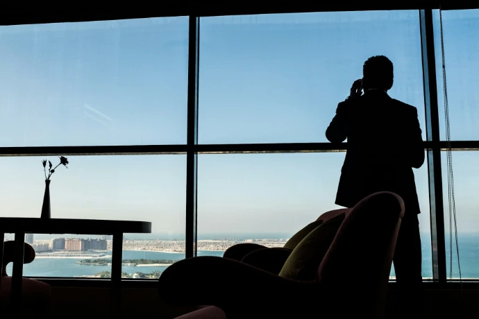 Man in suit talking on phone by large window.